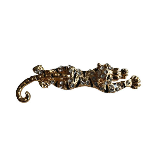 A gold-toned leopard-shaped brooch embellished with clear rhinestones, resting on a plain light gray surface.