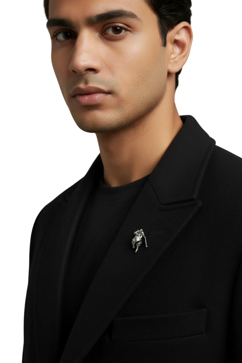 Man wearing a black blazer with a distinctive lapel pin against a neutral background