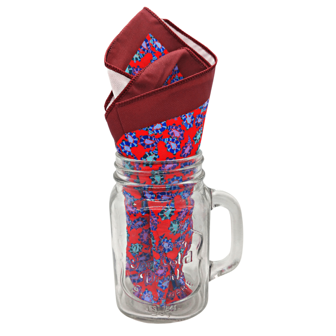 A red pocket square with a floral pattern displayed inside a clear glass mug.