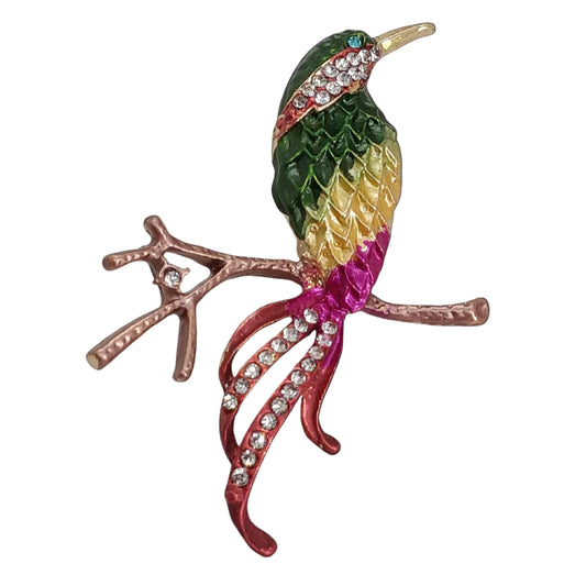 A colorful brooch designed in the shape of a bird with a combination of green, yellow, red, and blue feathers, sitting on a branch.